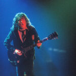 Angus Young of AC/DC playing electric guitar on stage in a school uniform