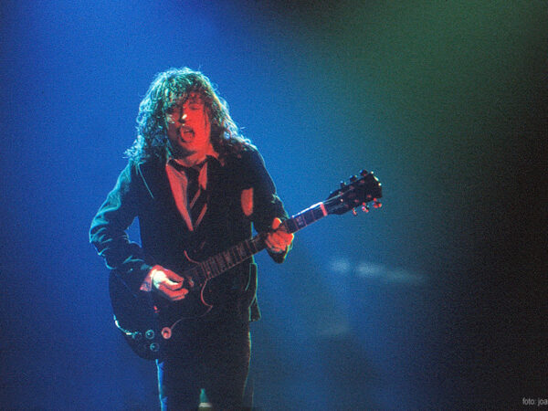 angus_young_acdc Angus Young of AC/DC playing electric guitar on stage in a school uniform