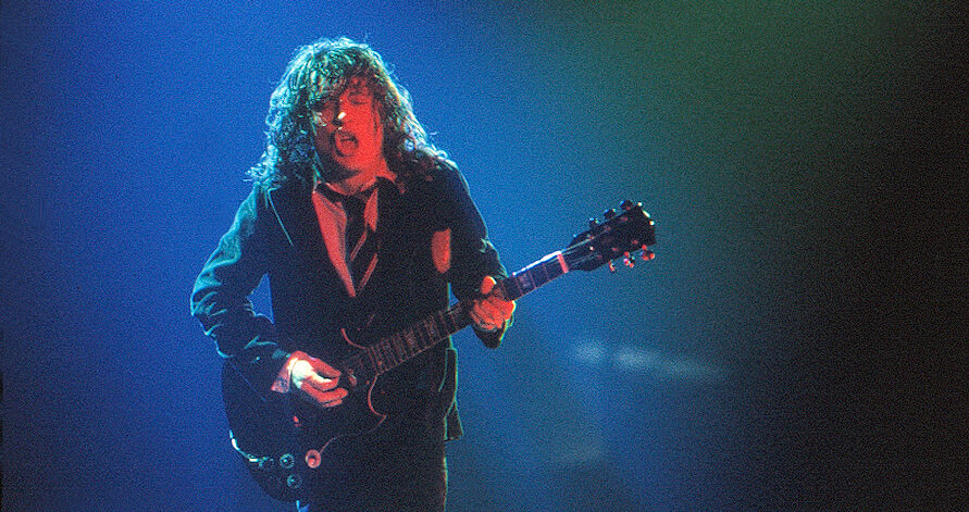 Angus Young of AC/DC playing electric guitar on stage in a school uniform