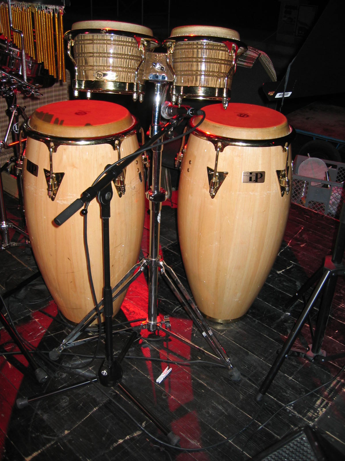 Pair of conga drums beside bongo drums against a plain background