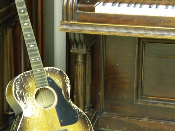 Acoustic guitar standing in front of a vintage upright piano