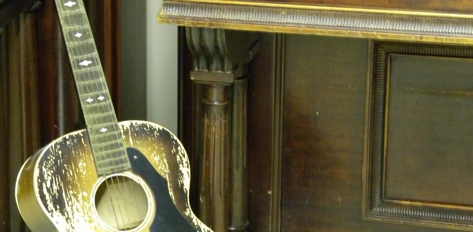 Acoustic guitar standing in front of a vintage upright piano