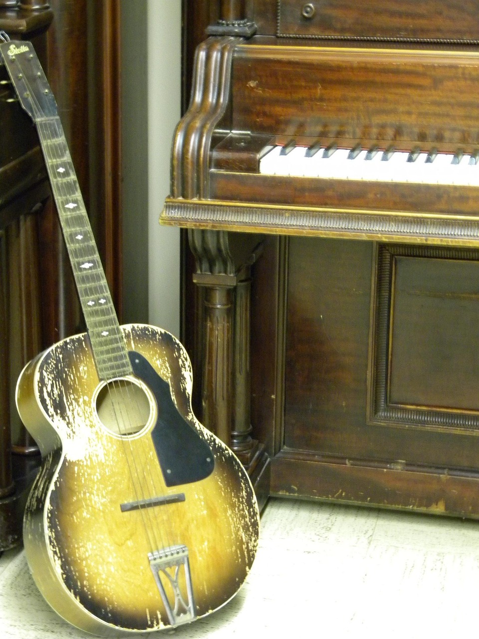 Acoustic guitar standing in front of a vintage upright piano