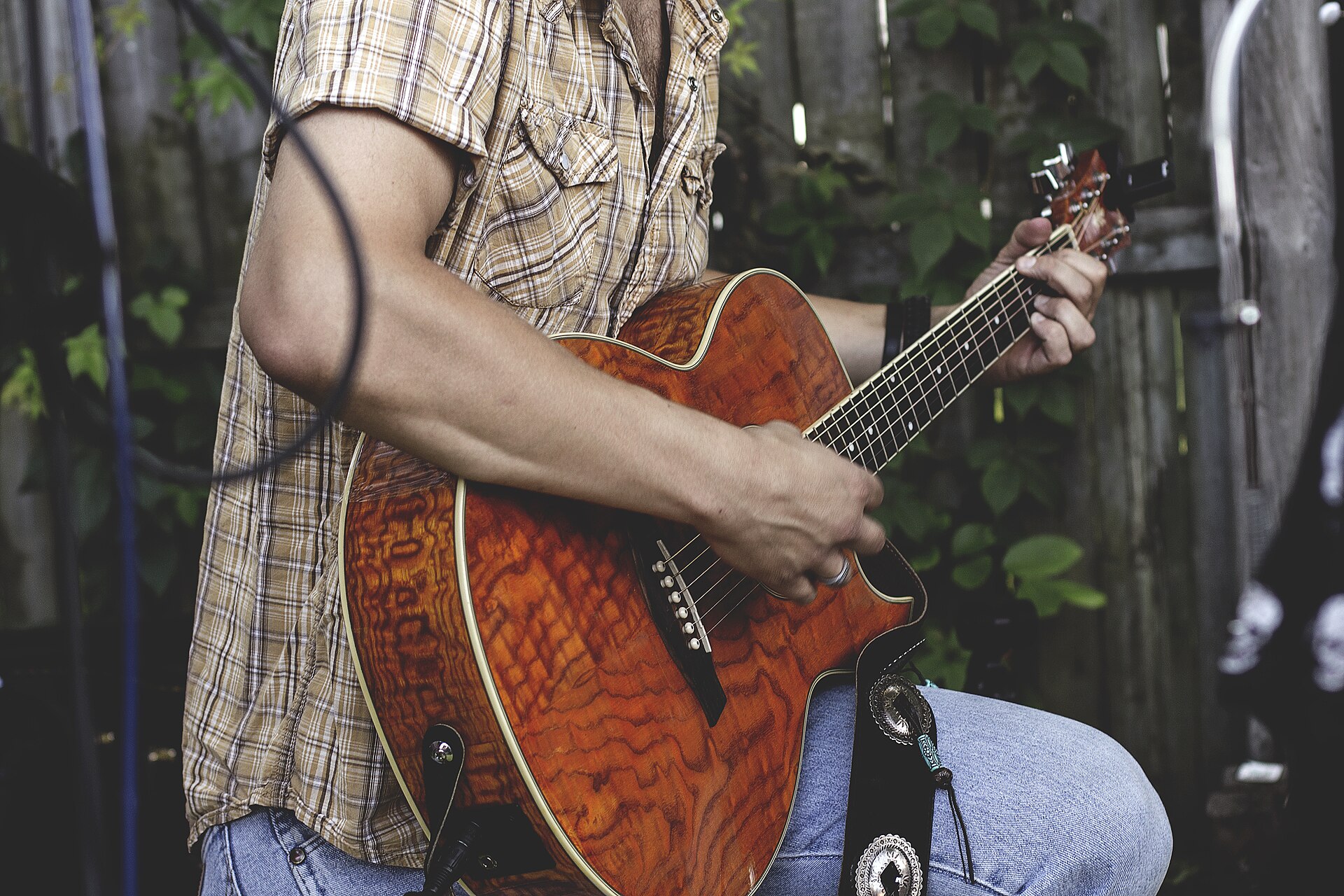 Person sitting outdoors in a garden playing an acoustic guitar