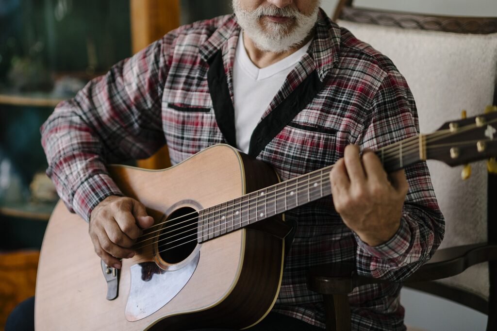 Older adult practising acoustic guitar while seated