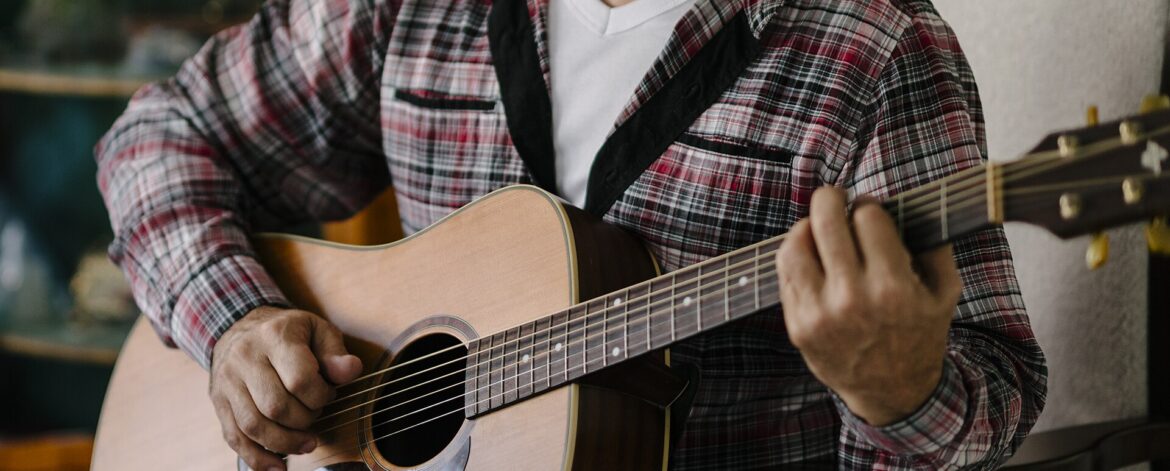 Older man plays acoustic guitar while sitting in a chair Older adult man sitting in a chair and playing an acoustic guitar
