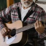 Older adult man sitting in a chair and playing an acoustic guitar