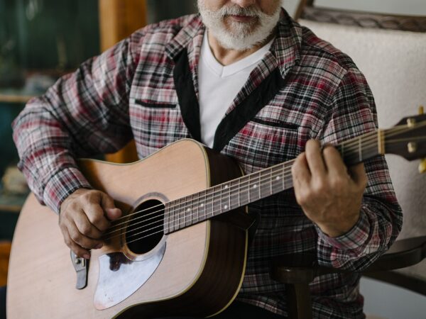 Older man plays acoustic guitar while sitting in a chair Older adult man sitting in a chair and playing an acoustic guitar