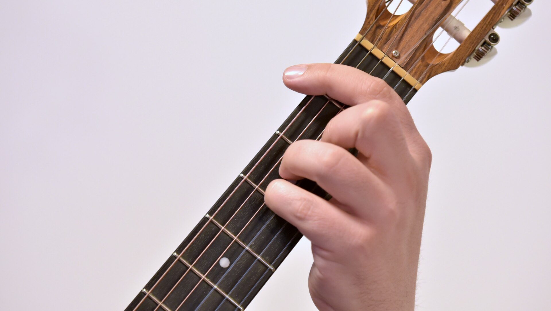 A hand holding an A sharp minor barre chord on a classical guitar neck, showing how to play barre chords