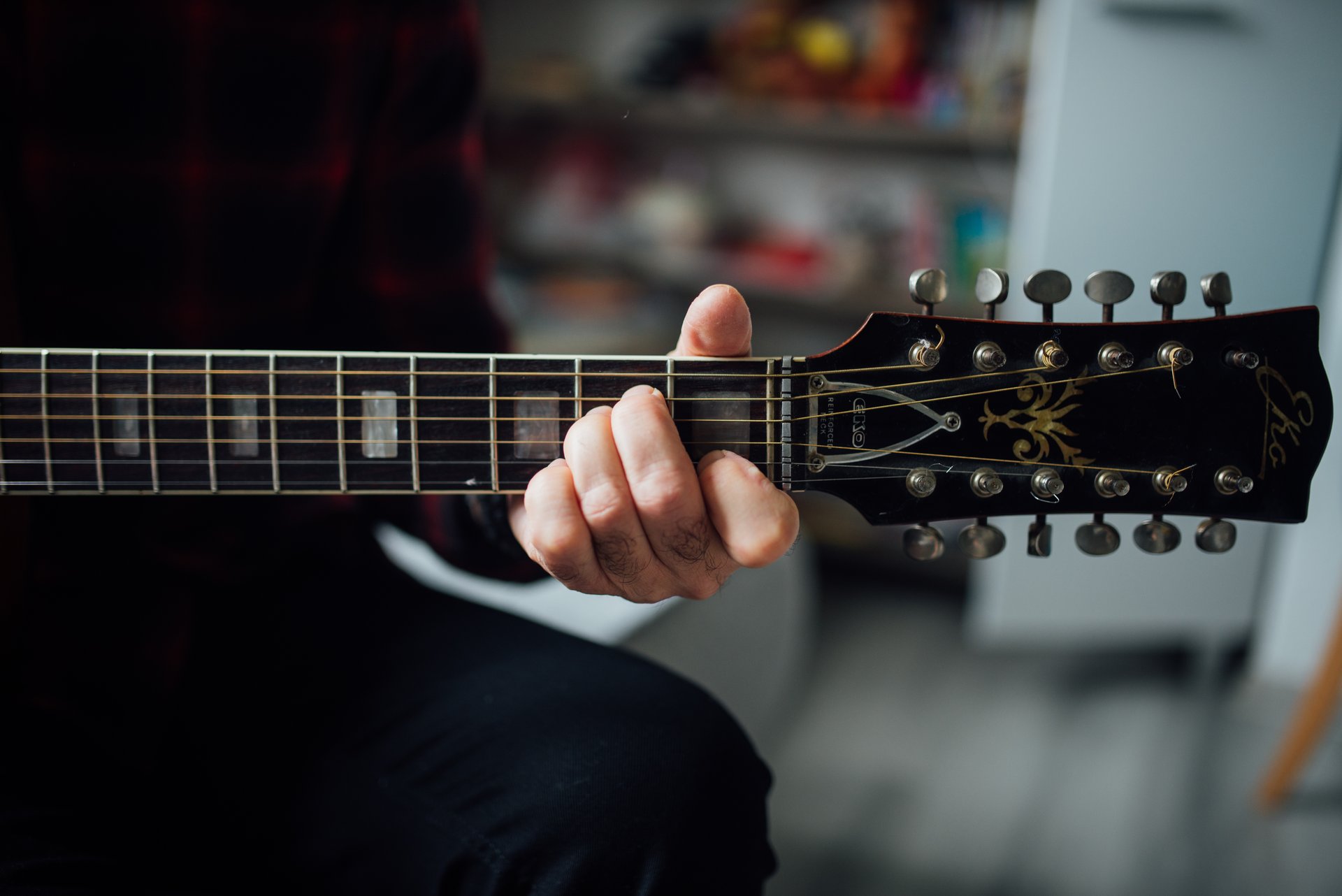 Close view of a fretting hand holding a chord on an acoustic guitar neck, showing thumb and wrist position