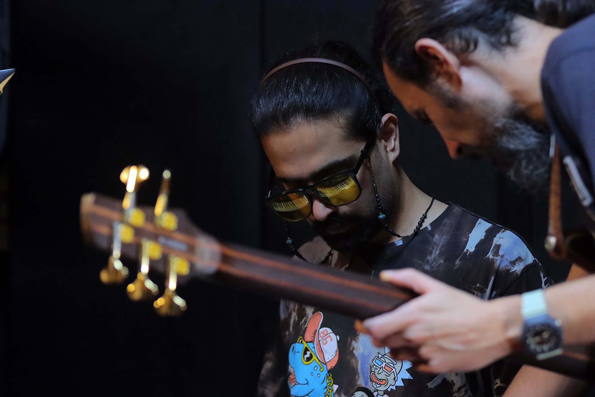 Two men looking closely at the neck of a guitar together