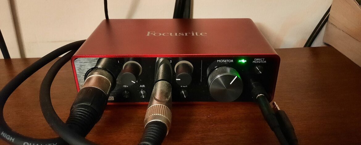 Home recording setup for guitar: a red Focusrite Scarlett Solo (3rd Gen) audio interface on a desk with an XLR lead and a guitar lead plugged in