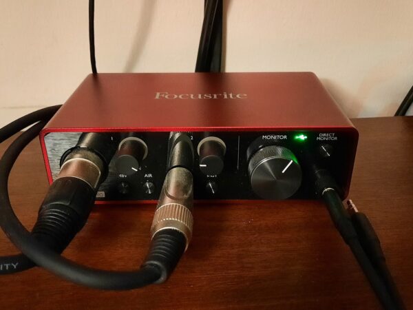 Home recording setup for guitar: a red Focusrite Scarlett Solo (3rd Gen) audio interface on a desk with an XLR lead and a guitar lead plugged in
