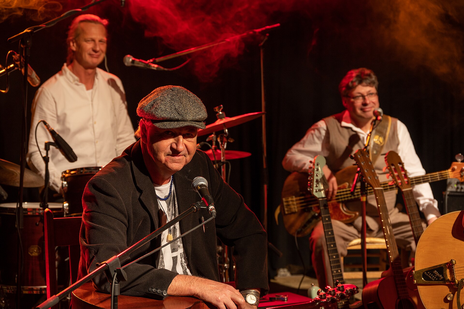 A band playing a stage show that is being streamed live online, with microphones and a guitar in the foreground