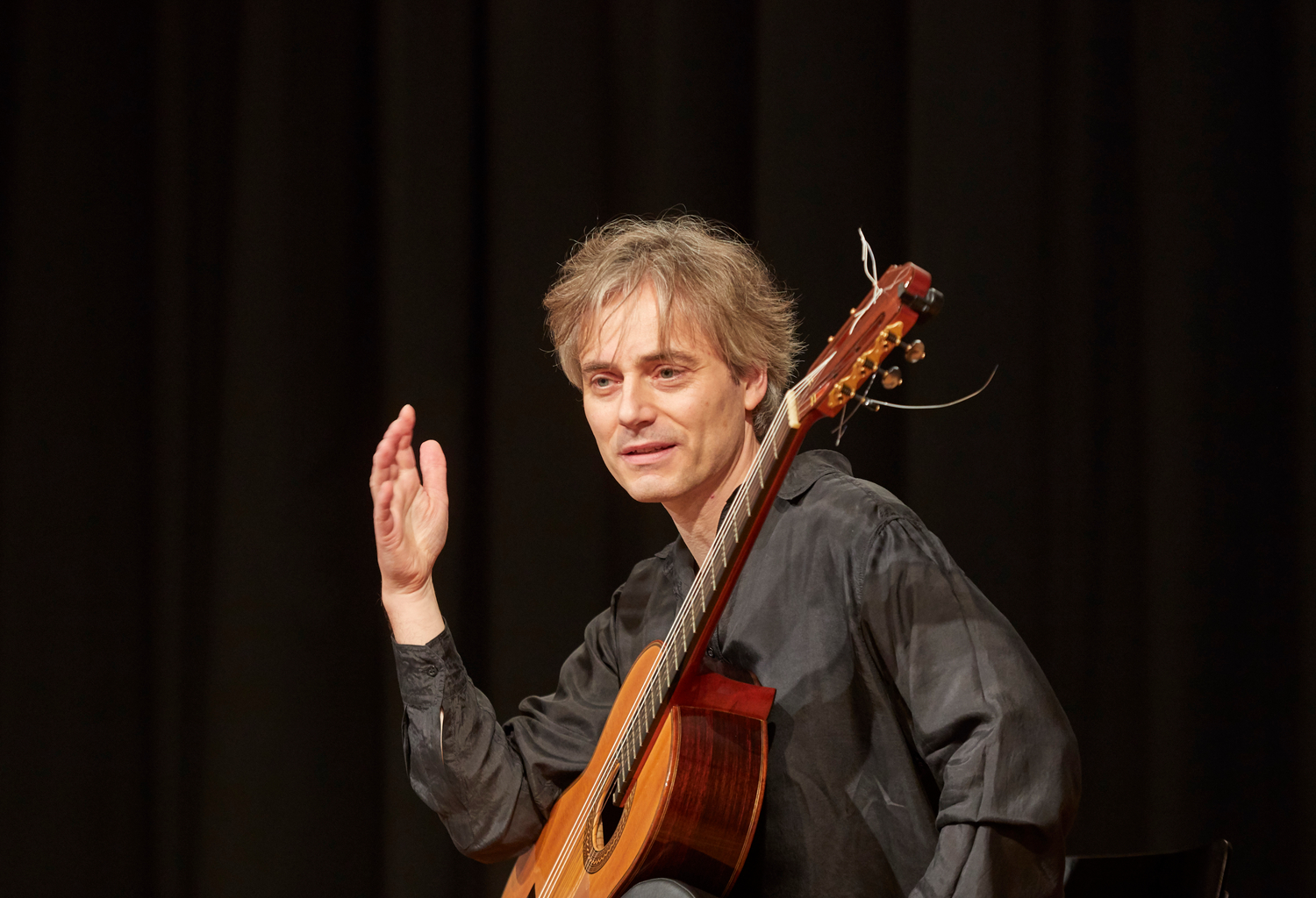 A guitarist talking to the audience during a live concert, the side by side of gigs and online for a guitarist