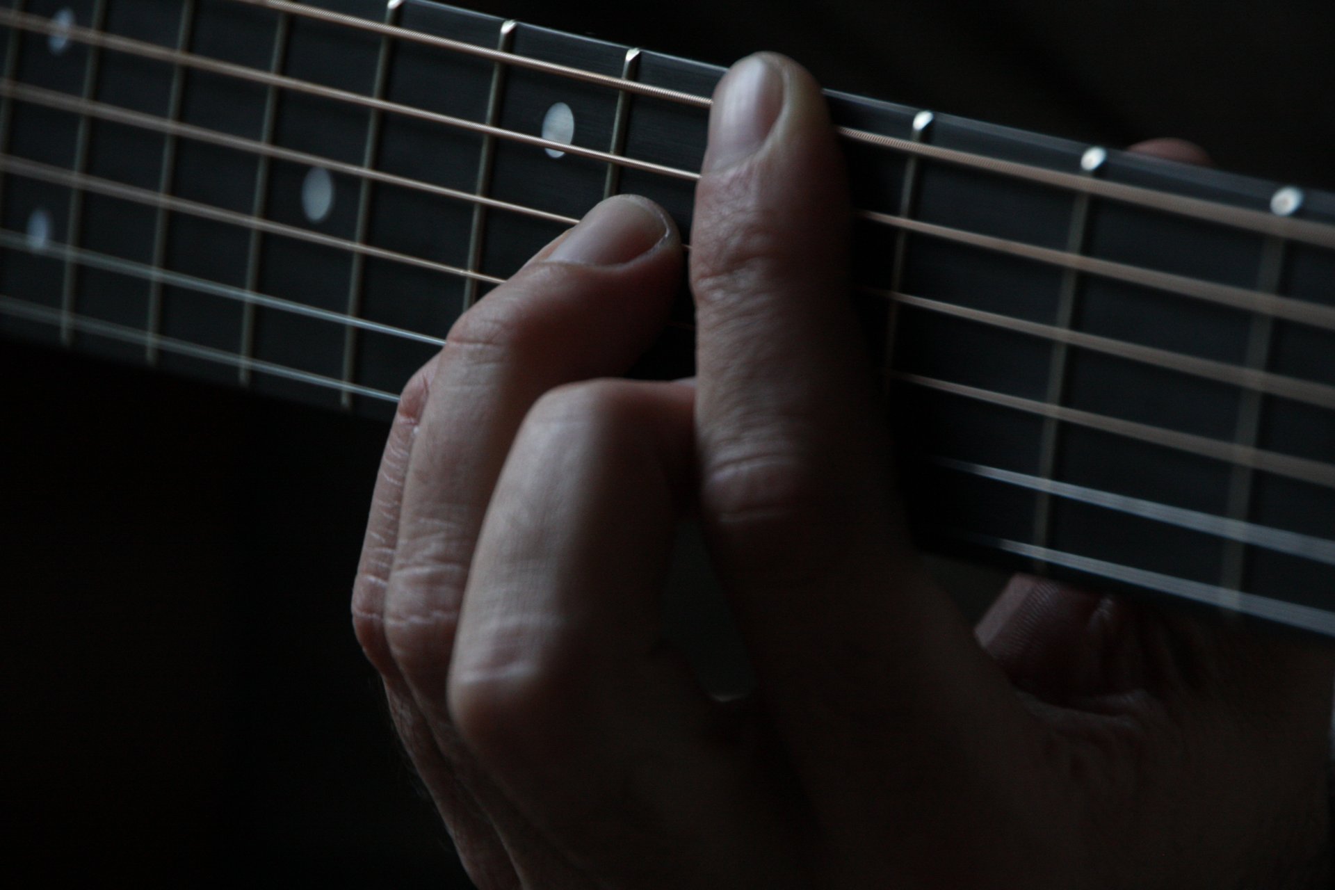 Fretting hand resting lightly on a guitar fretboard with fingers placed just behind the frets