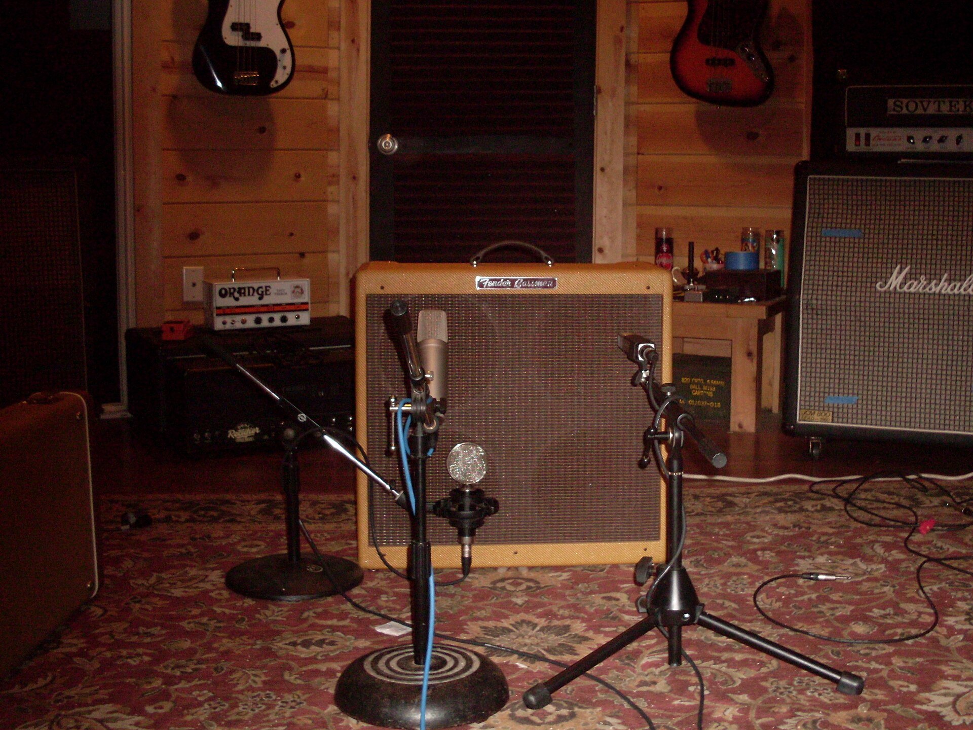 Two microphones on stands set up in front of a tweed Fender combo amp in a wood panelled recording room