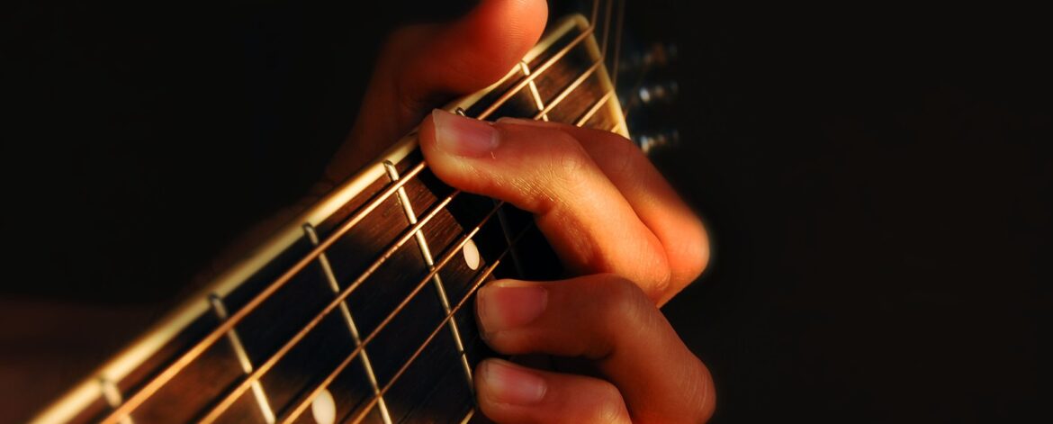 Fingertips pressing the strings of an acoustic guitar, where sore fingertips from guitar usually start.