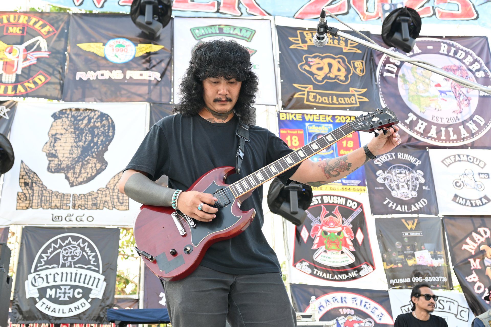 Guitarist standing on an outdoor stage playing a red electric guitar on a strap at about waist height