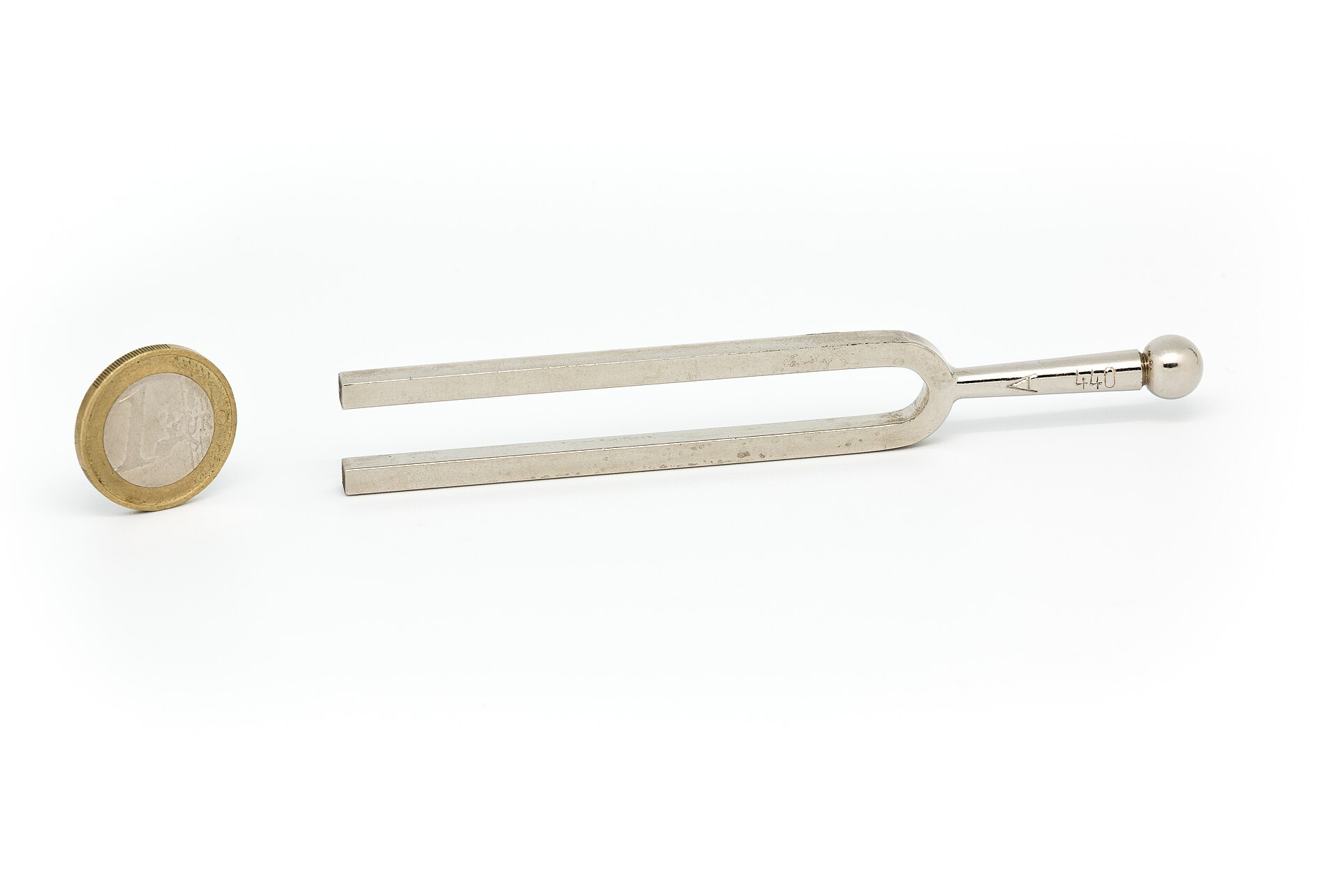 Steel tuning fork marked 440 Hz lying next to a coin, a simple reference pitch for tuning a guitar