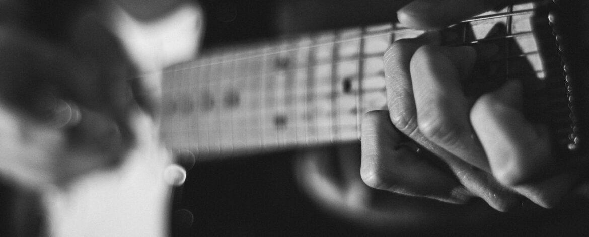 web_fretboard_chord_black_white Guitarist fretting a chord, the first step in learning songs with common chord progressions by ear