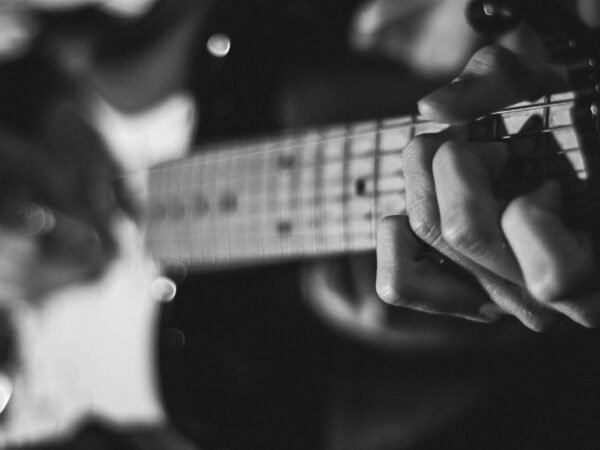 web_fretboard_chord_black_white Guitarist fretting a chord, the first step in learning songs with common chord progressions by ear