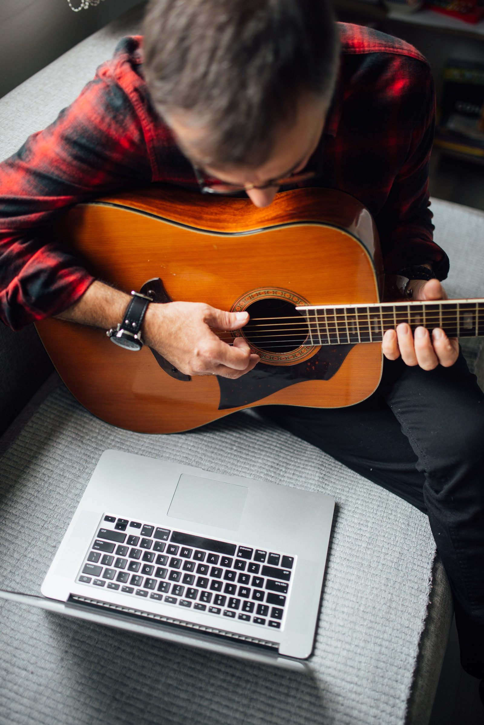 Guitarist with an acoustic guitar working on a laptop at home