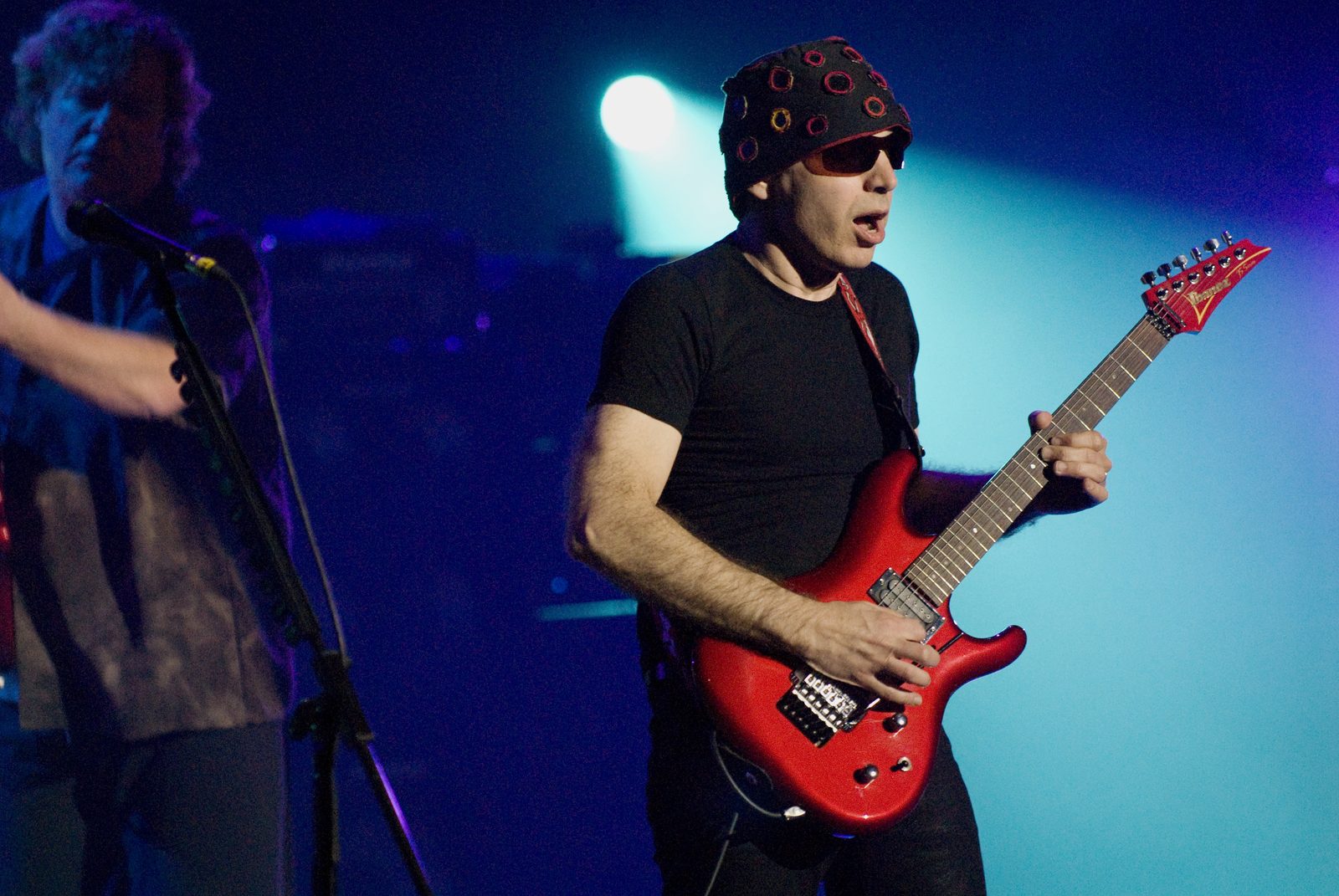 Joe Satriani playing a red guitar on stage in 2008