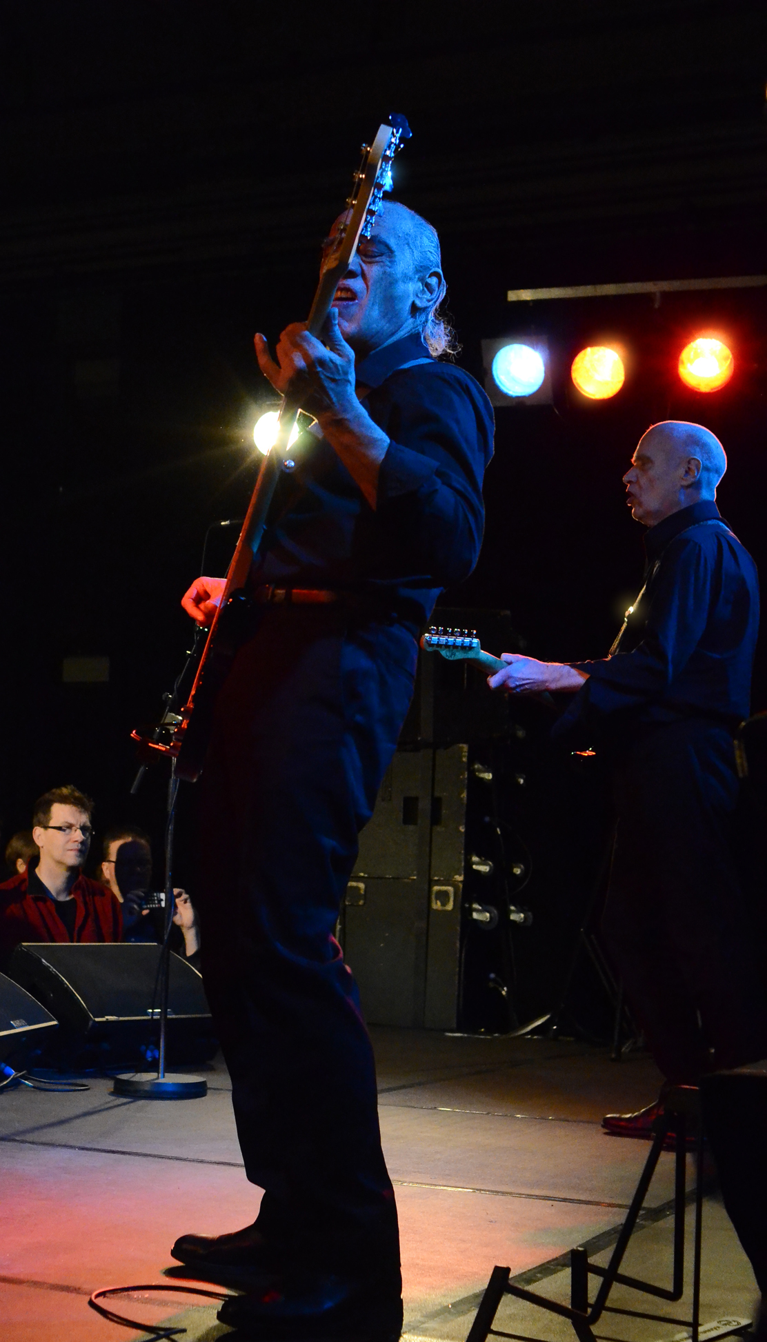 Wilko Johnson raising his guitar like a gun on stage with Norman Watt Roy on bass in 2014